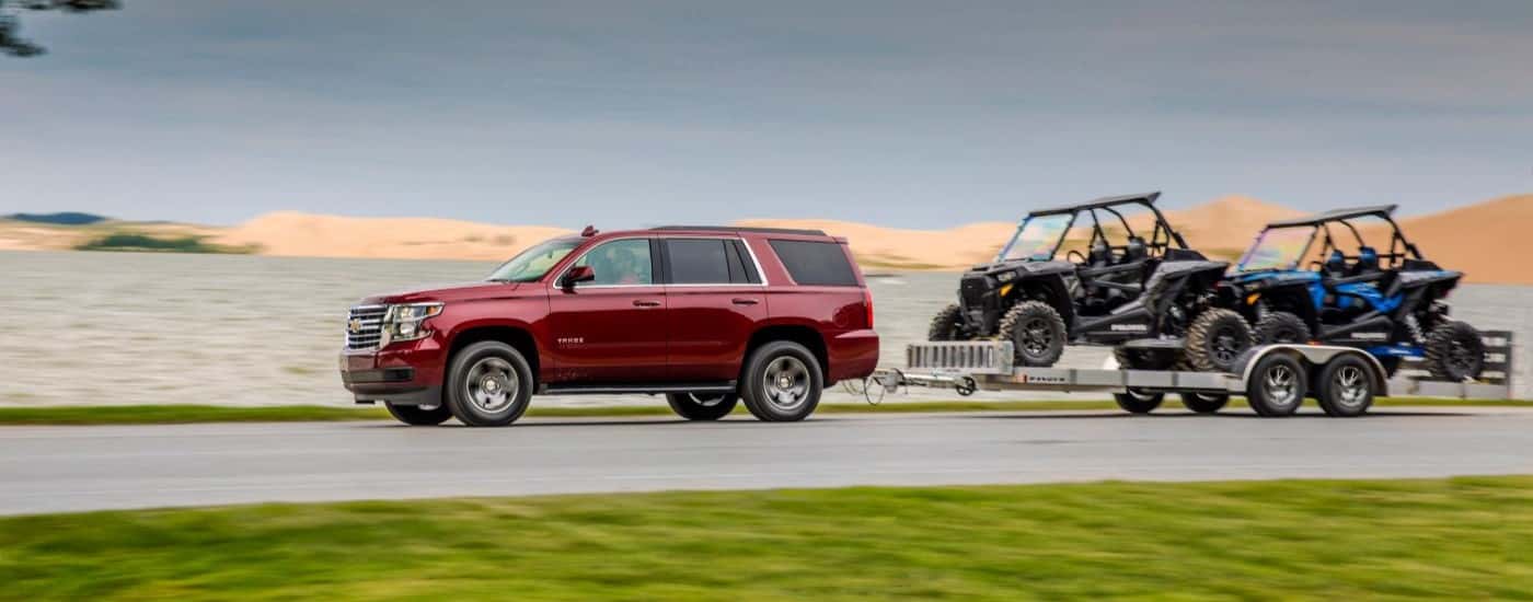 Red 2018 Chevy Tahoe towing ATVs down a road.
