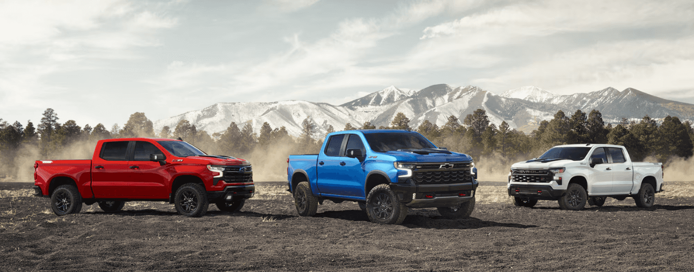 A red 2026 Chevy Silverado 1500 Z71, a blue Chevy Silverado 1500 ZR2, and a white 2026 Chevy Silverado ZR2 Bison parked side by side off-road