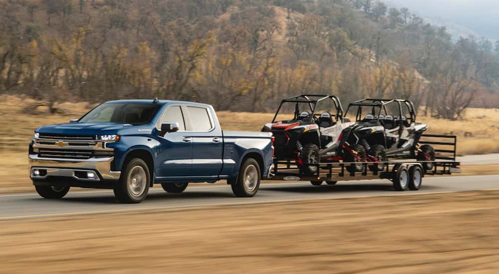 Blue 2021 Chevy Silverado 1500 towing a trailer with ATVs on it