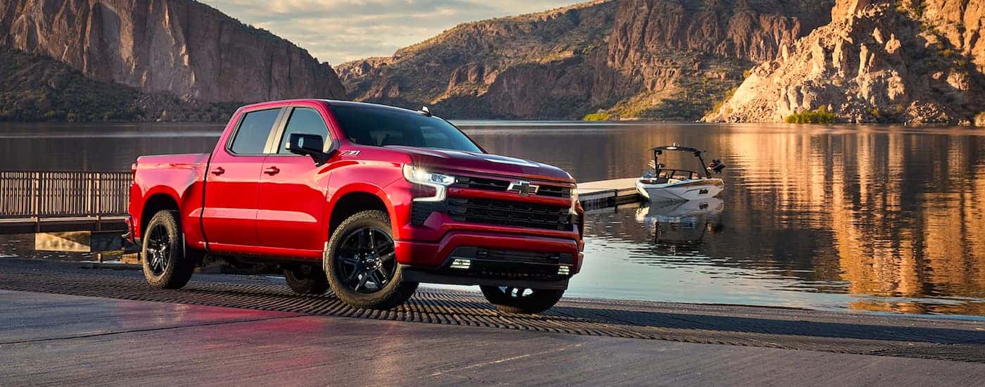 Red 2022 Chevy Silverado 1500 parked on a lake with a boat in the water