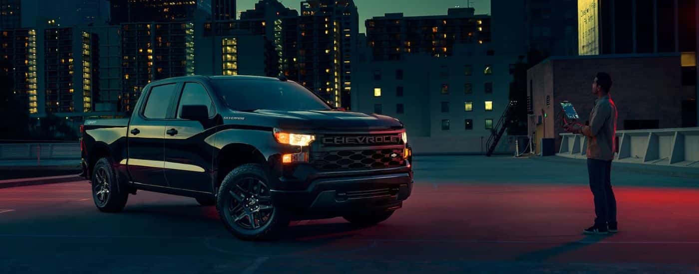 Black 2023 Chevy Silverado 1500 parked at night with city lights in the background