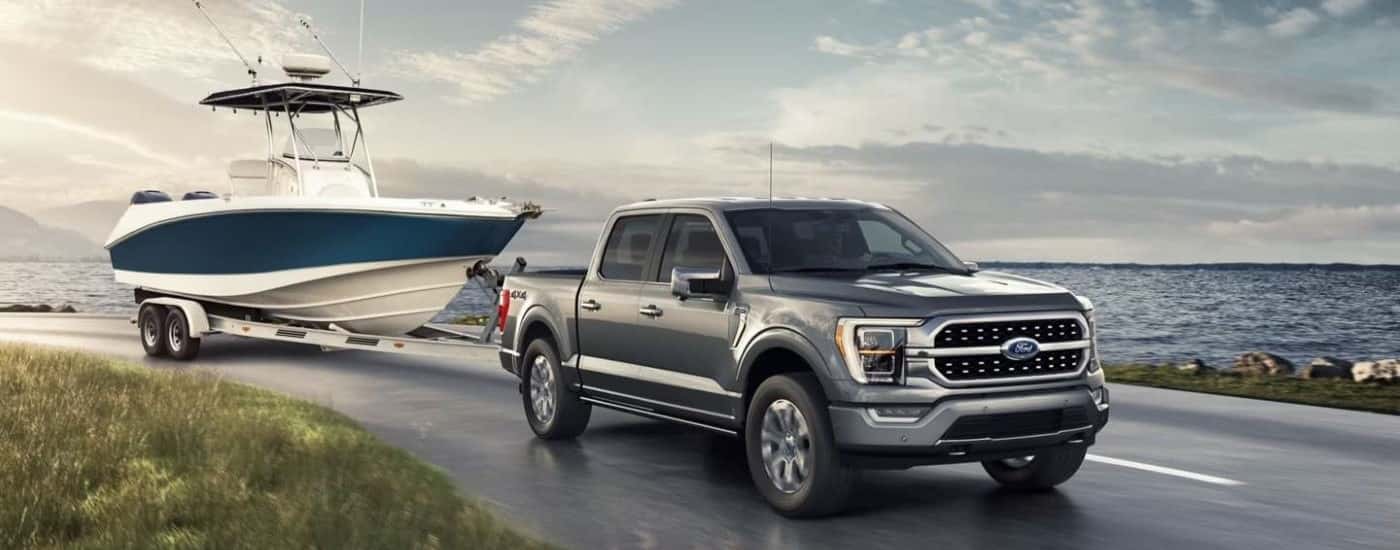 Grey Ford F-150 towing a boat along a lake road.