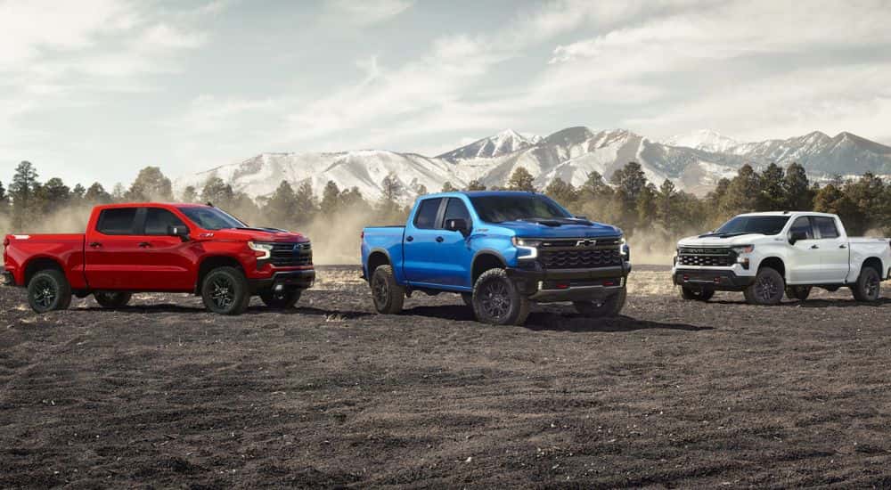 Three 2024 Chevy Silverado trucks - red, blue and white - parked in front of mountains.