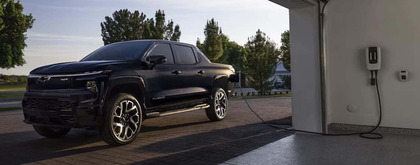 A black 2023 Chevy Silverado EV plugged in to charge in a home garage.