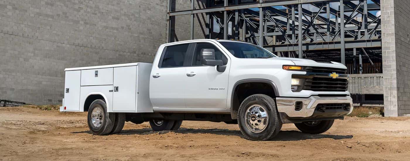 A white 2026 Chevy Silverado 3500 HD Chassis Cab with a utility bed parked at a construction site.