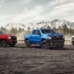 Three 2024 Chevy Silverado trucks - red, blue and white - parked in front of mountains.