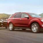 Red 2016 Chevy Equinox towing jet skis by a lake.