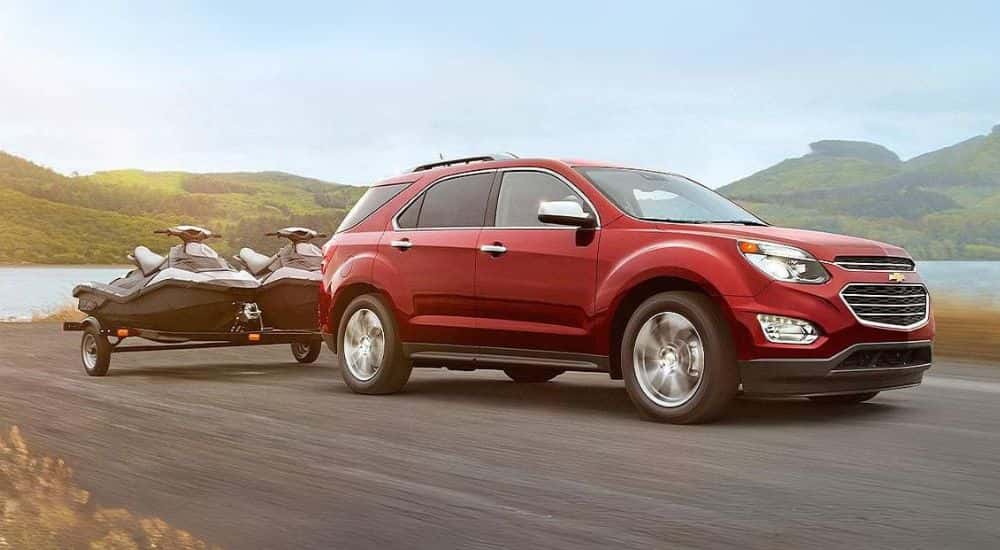 Red 2016 Chevy Equinox towing jet skis by a lake.
