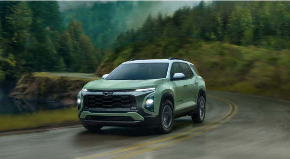 Green 2025 Chevy Equinox driving on a road in the woods.