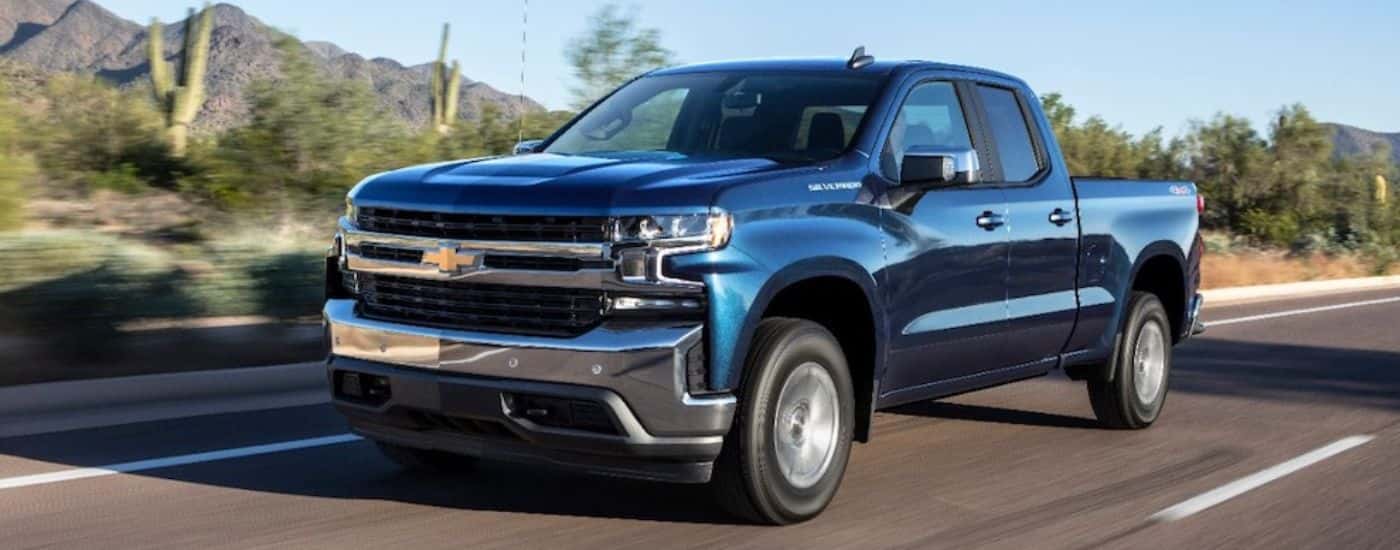 Blue 2019 Chevrolet Silverado driving on a paved road by cacti.