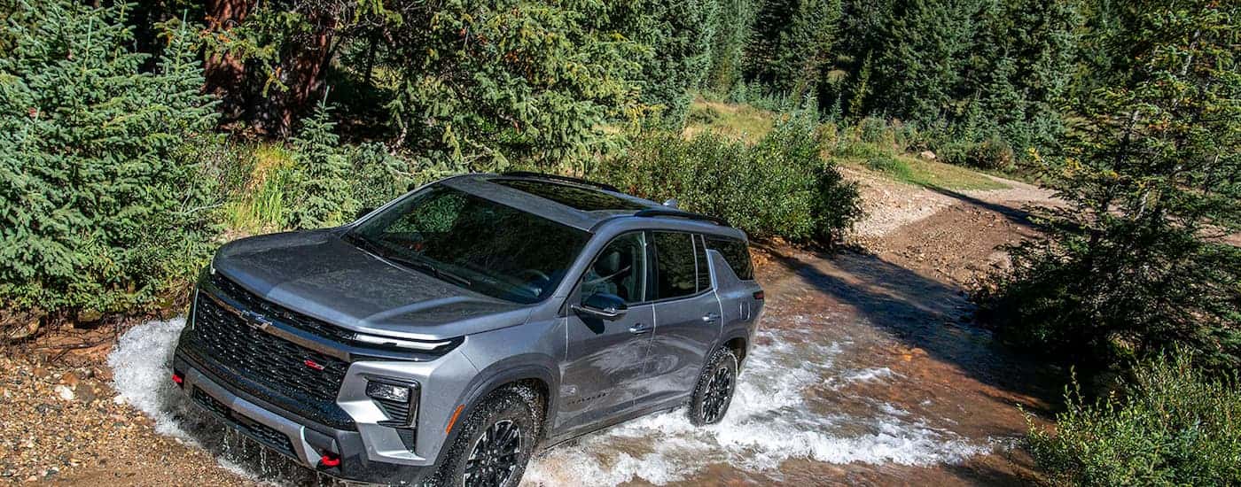 A silver 2026 Chevy Traverse RS off-roading in a stream