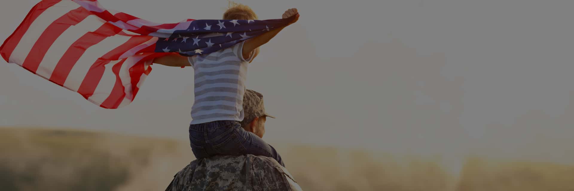 man in military uniform carrying child with american flag