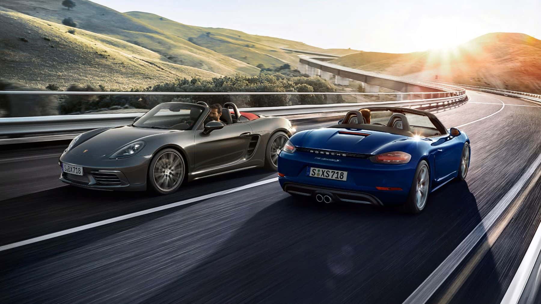 Two 2025 Porsche 718 Boxster models driving opposite directions on the highway