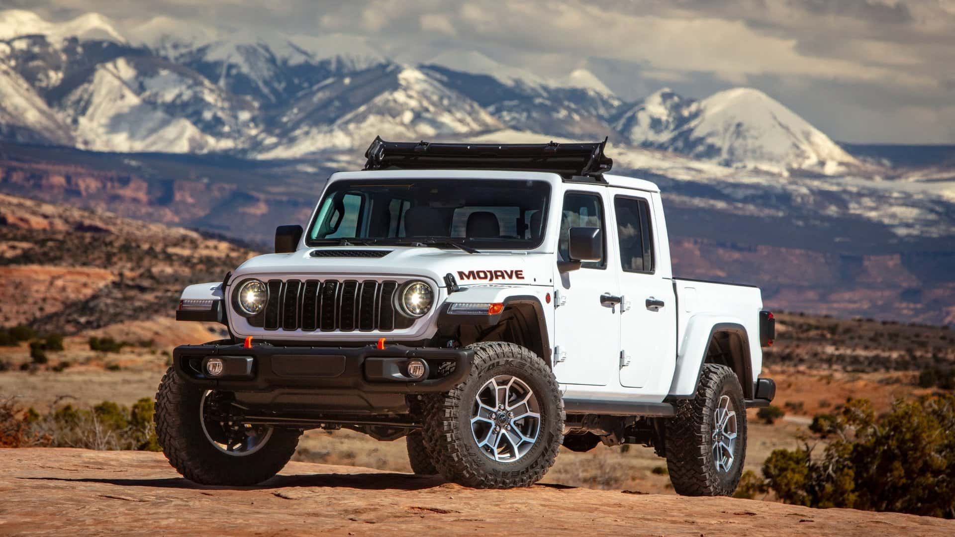 2026 Jeep® Gladiator Mojave white off-road pickup shown on rocky terrain with snowy mountains behind