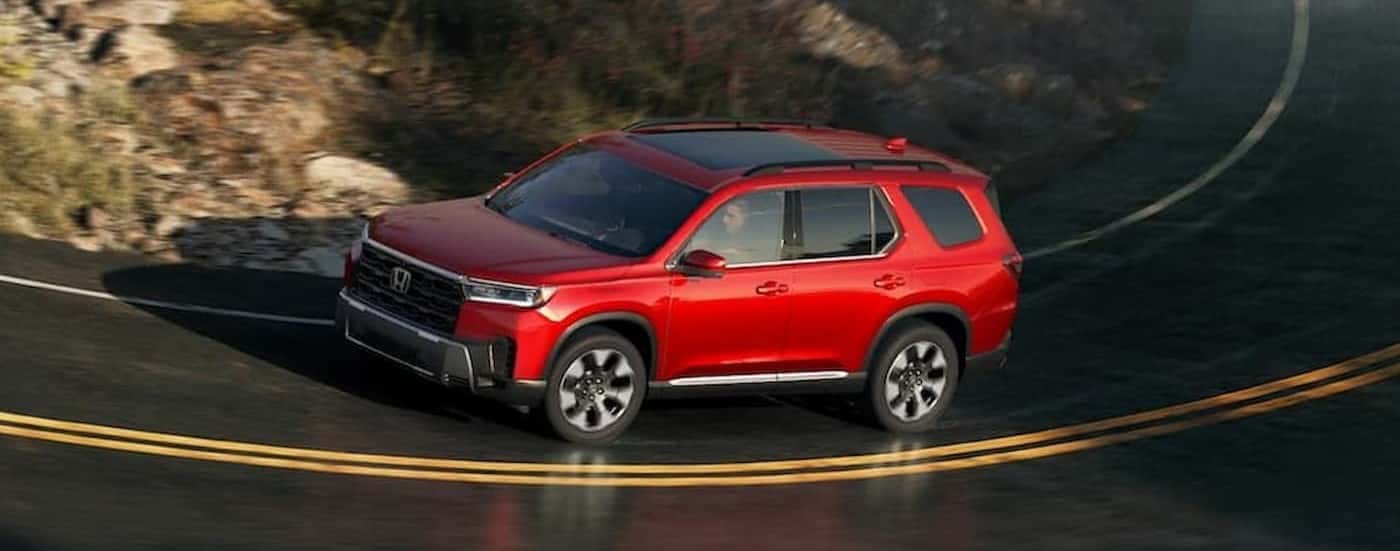 A red 2026 Honda Pilot driving on a highway.