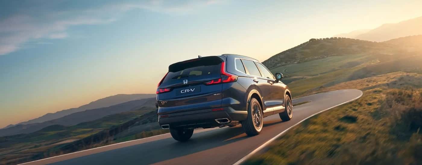 Rear of a black 2026 Honda CR-V Hybrid driving down a road.