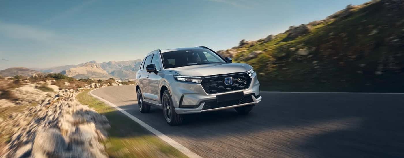 White 2026 Honda CR-V Hybrid driving down a road.