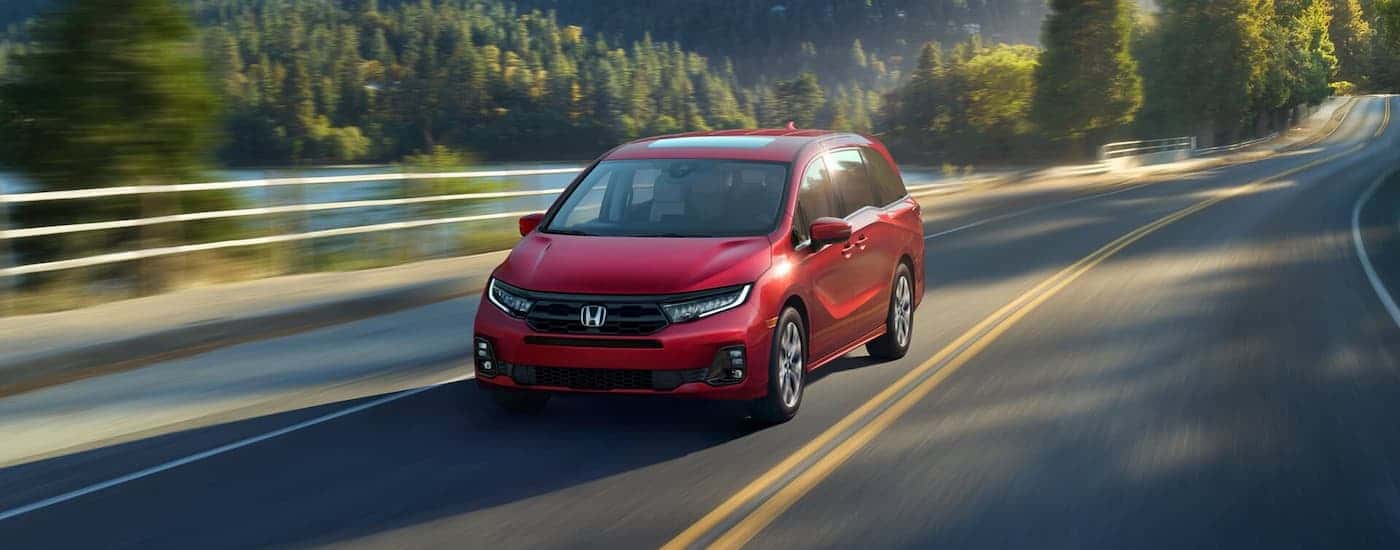 Red 2026 Honda Odyssey driving down a road.