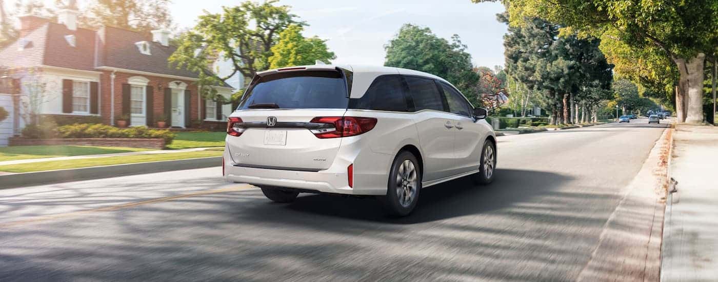 Rear of a white 2026 Honda Odyssey driving down a neighborhood street.