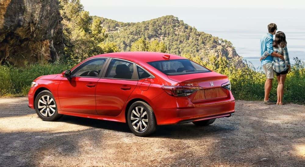 A red 2026 Honda Civic Sedan parked by a scenic view and two people.