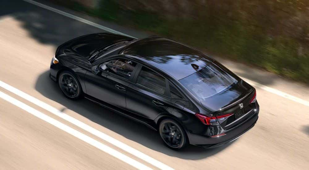 Black 2026 Honda Civic Sport driving down a road.