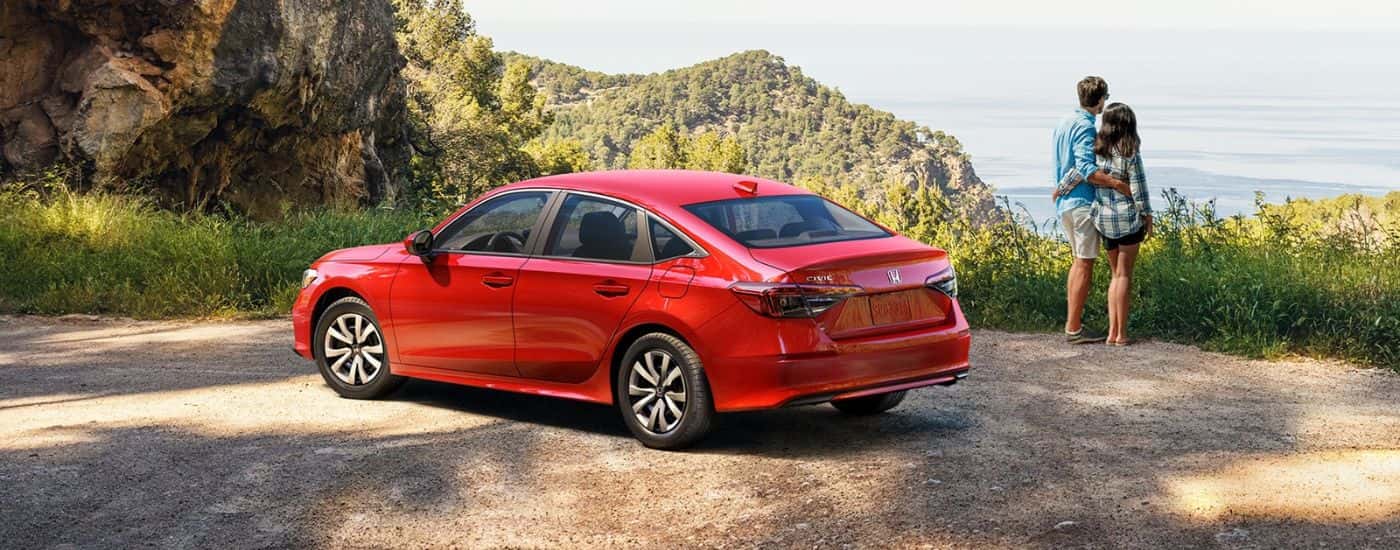 A red 2026 Honda Civic Sedan parked by a scenic view and two people.