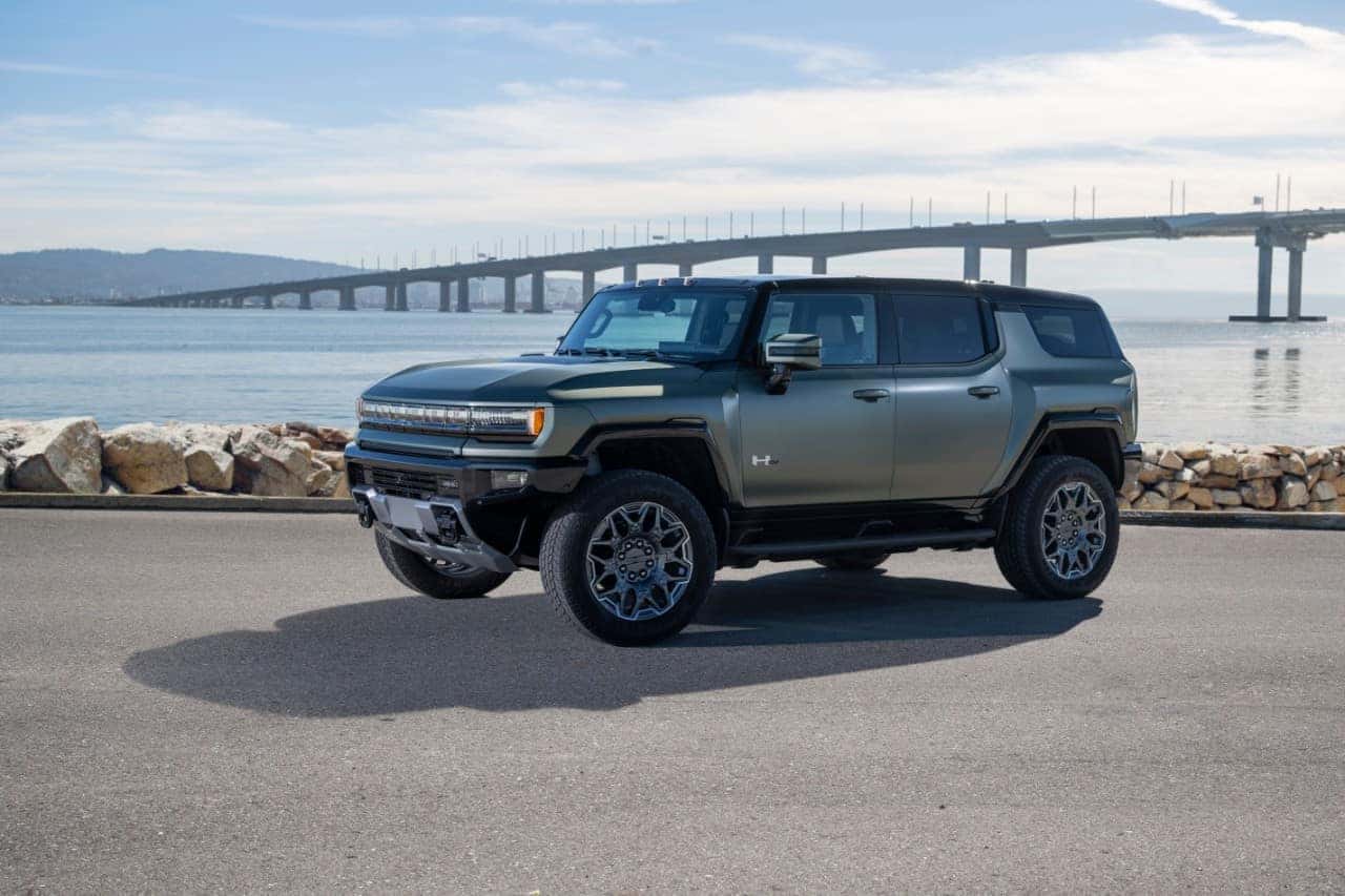 2024 GMC HUMMER EV SUV in Moonshot Green Matte parked near water and a bridge.