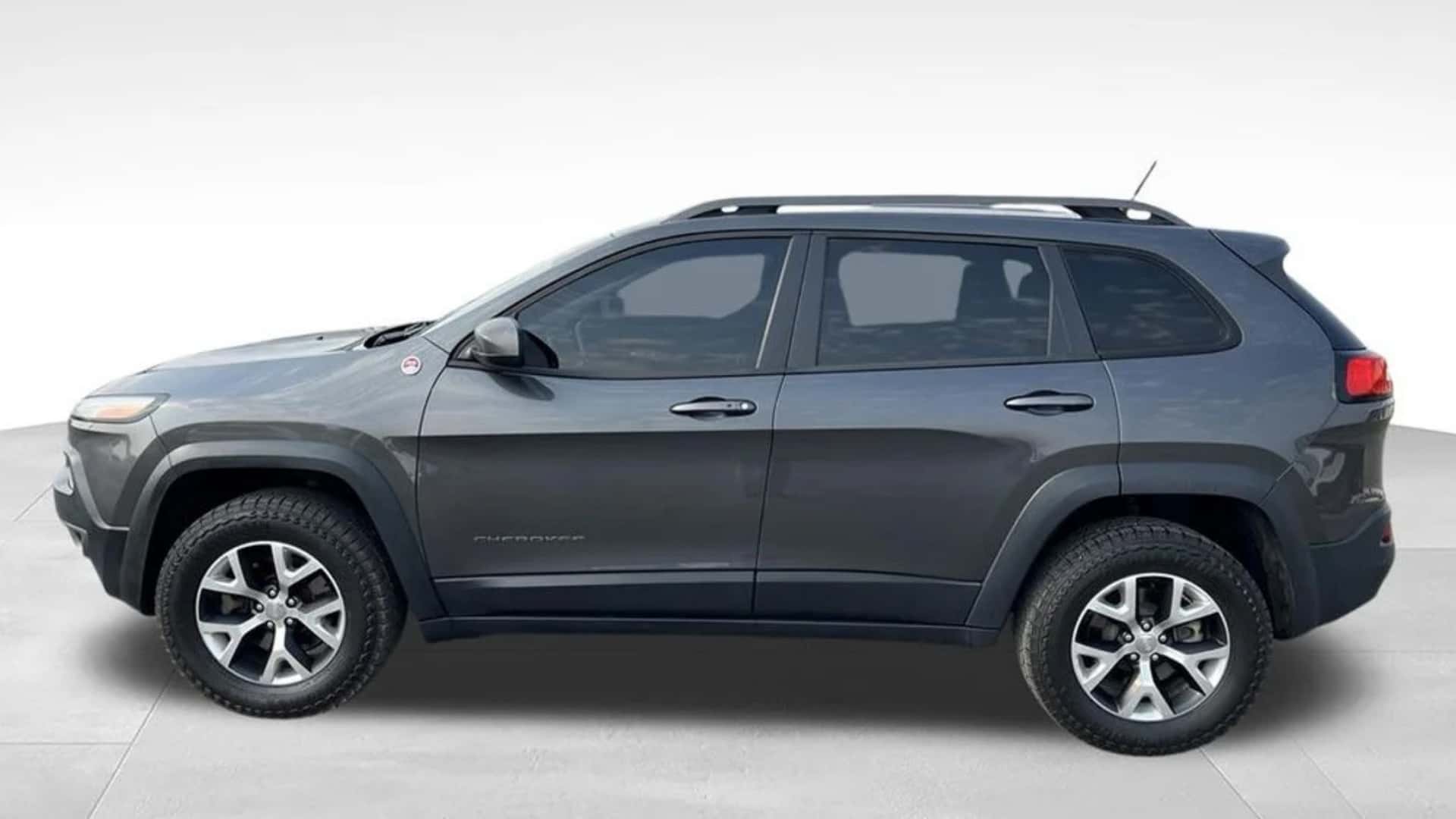 Dark gray Jeep Cherokee side profile with roof rails, rugged tires, and clean studio-style vehicle background.