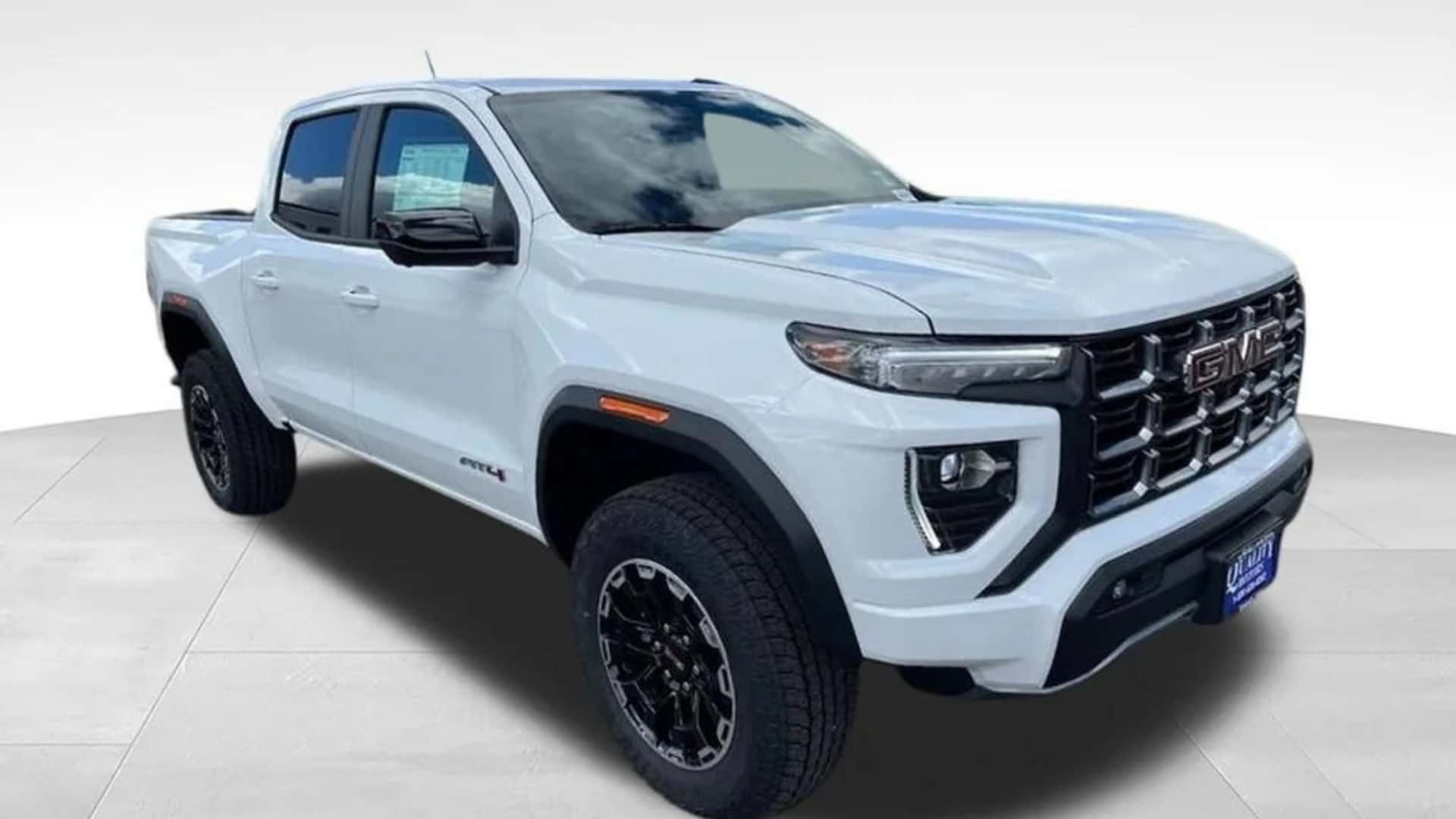 White GMC Canyon pickup front three-quarter view with bold GMC grille, black wheels, and crew cab design.