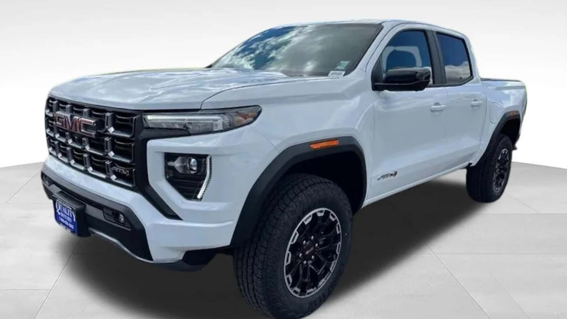 White GMC Canyon pickup front three-quarter view with bold grille, black wheels, crew cab, and rugged truck stance.