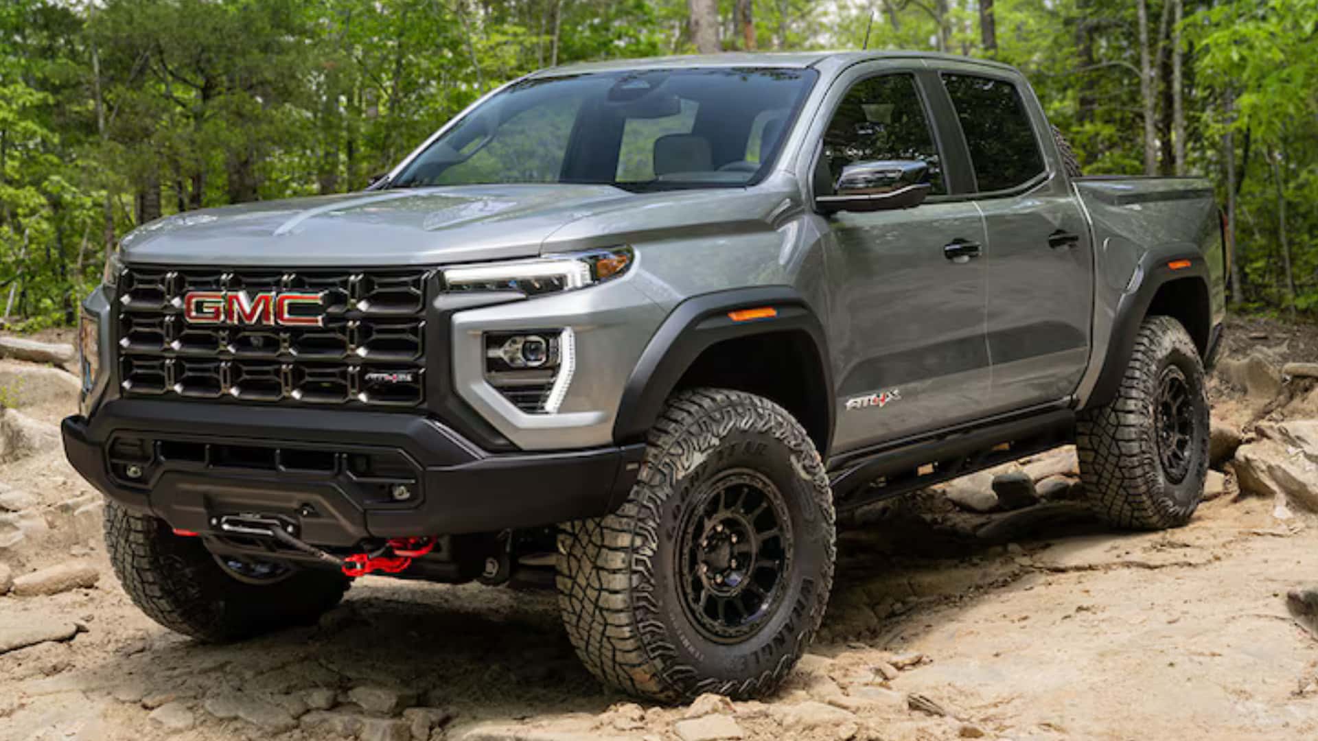 Gray GMC Canyon AT4X off-road pickup on rocky terrain with all-terrain tires, lifted stance, and rugged front bumper.