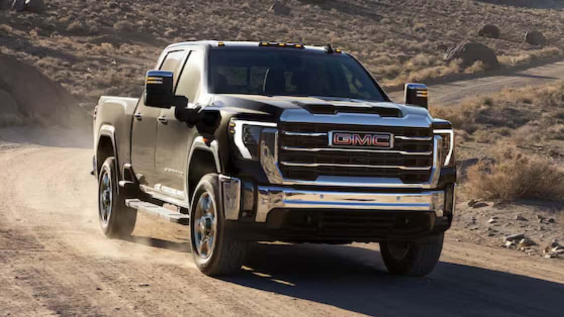 Black GMC Sierra HD truck driving on a dusty desert road with chrome grille, tow mirrors, and rugged stance.