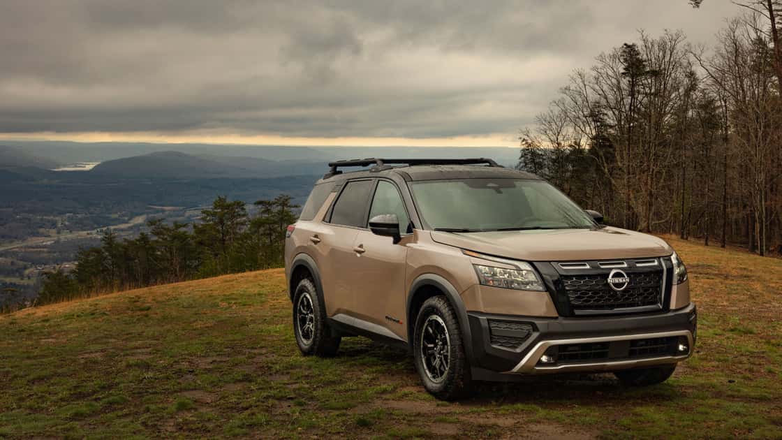 Nissan Pathfinder® SUV parked on a mountain overlook with roof rails, rugged tires, and cloudy scenic background.