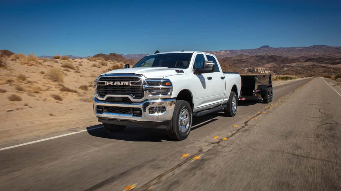 White Ram Heavy Duty truck towing a trailer on a desert highway with chrome grille and strong hauling capability.