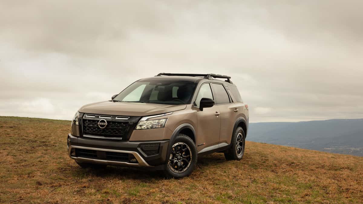 2025 Nissan Pathfinder® in bronze parked on a grassy overlook with roof rails and rugged outdoor styling.