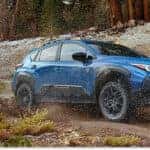 Front three-quarter view of a Geyser Blue 2026 Subaru Crosstrek Wilderness splashing mud on a snow-lined trail.