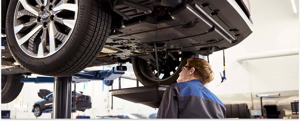 Subaru service technician draining oil from a vehicle elevated on a lift.