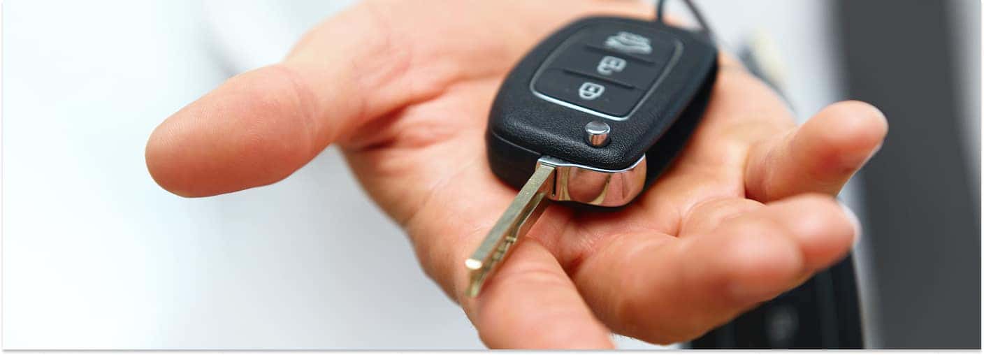 A close-up view of a person's open hand holding a black flip-style car key fob with the key blade extended against a bright, blurred background.