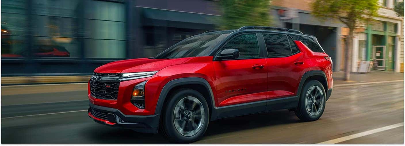A red 2026 Chevrolet Equinox drives down a city street, showcasing its sleek front three-quarter profile against a motion-blurred background.