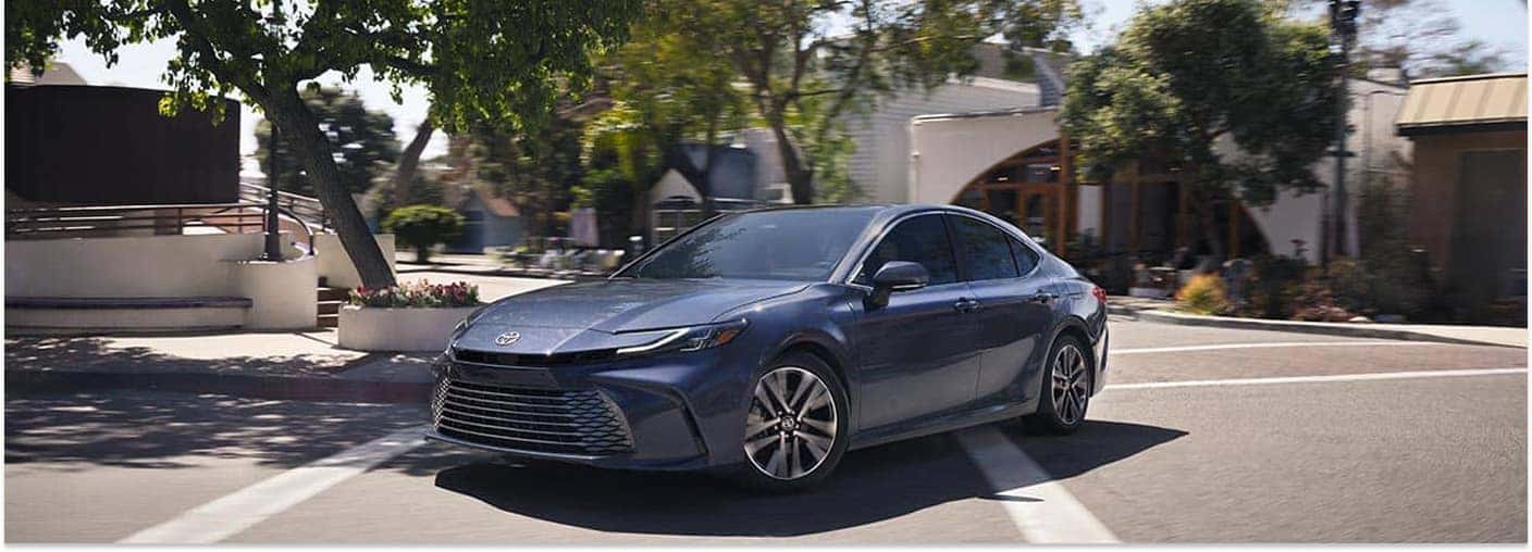 Front three-quarter view of a dark blue 2026 Toyota Camry driving on a town street.