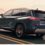 Rear three-quarter view of a dark gray 2026 Toyota RAV4 driving on a mountain road at sunset.
