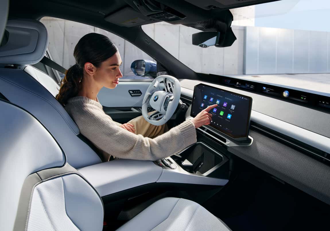 Driver interacts with BMW infotainment touchscreen inside a modern, upscale interior.