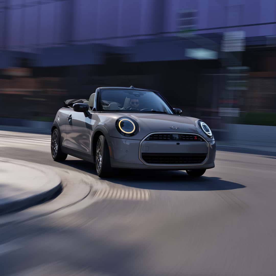 Gray MINI convertible driving through a city street.
