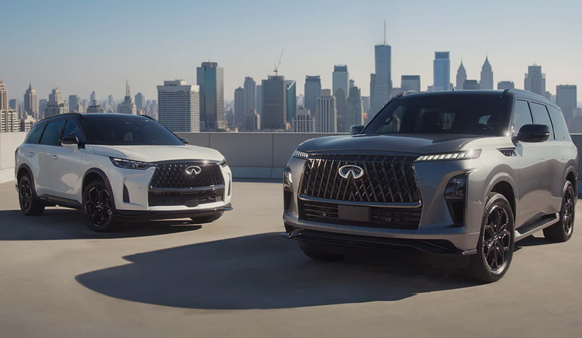 Two INFINITI SUVs parked on a rooftop with a city skyline in the background.