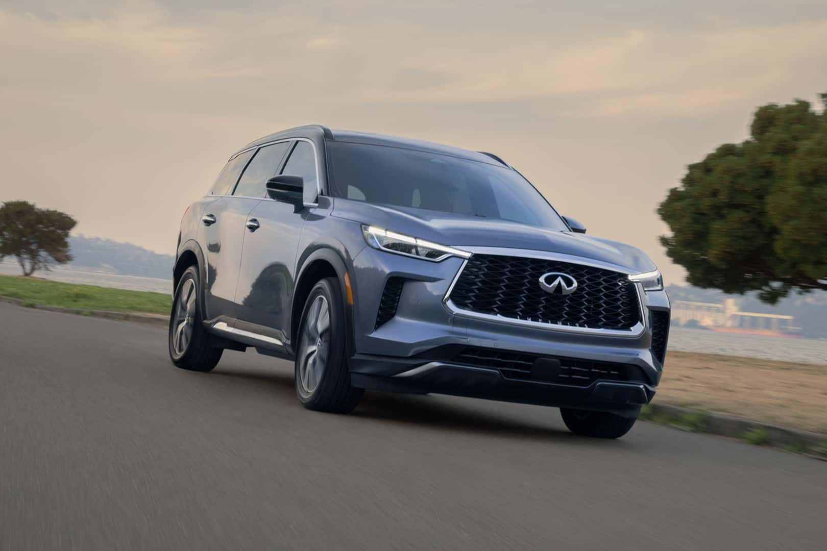 INFINITI QX60 driving on a paved road with soft background scenery.