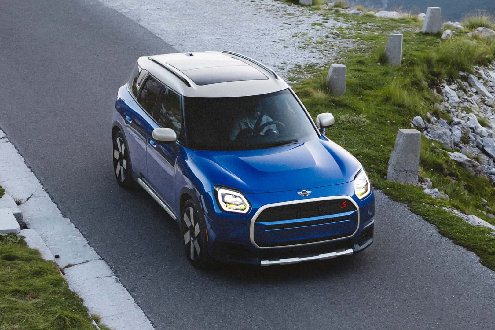 Blue MINI Countryman driving on a winding road through a scenic landscape.