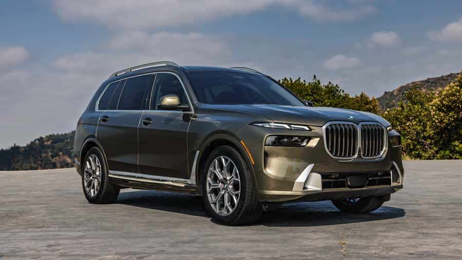 BMW X7 luxury SUV parked on a paved overlook with surrounding greenery and distant hills.