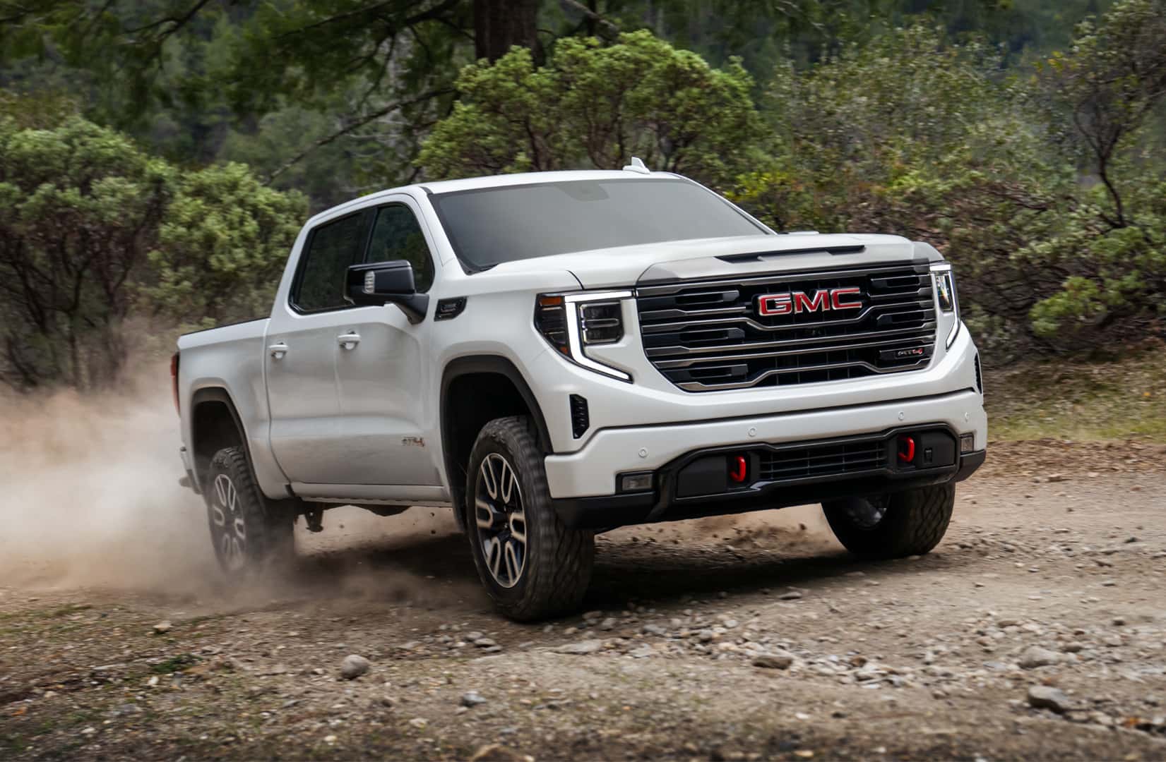 GMC Sierra driving on a dirt road among trees