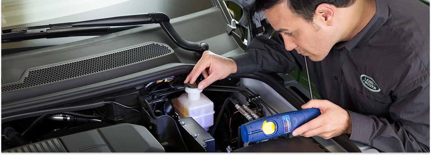 Land Rover technician inspecting fluid levels under the hood during routine vehicle maintenance.
