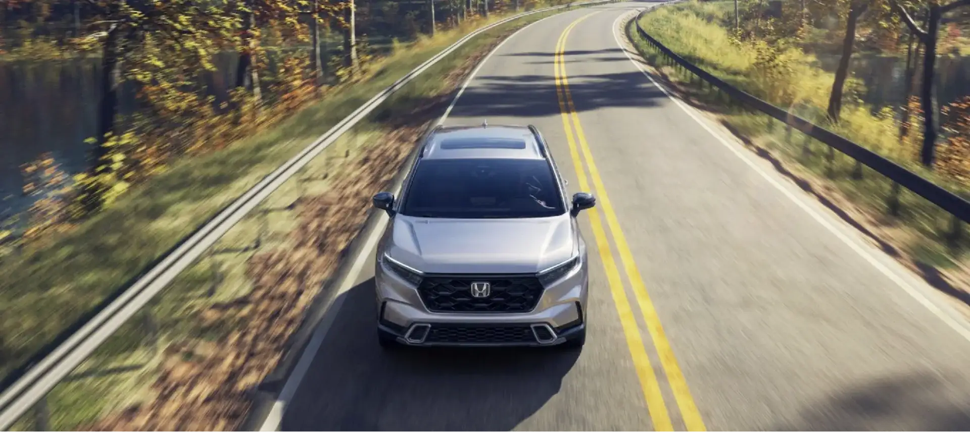 Honda CR-V driving along a winding tree-lined road in autumn